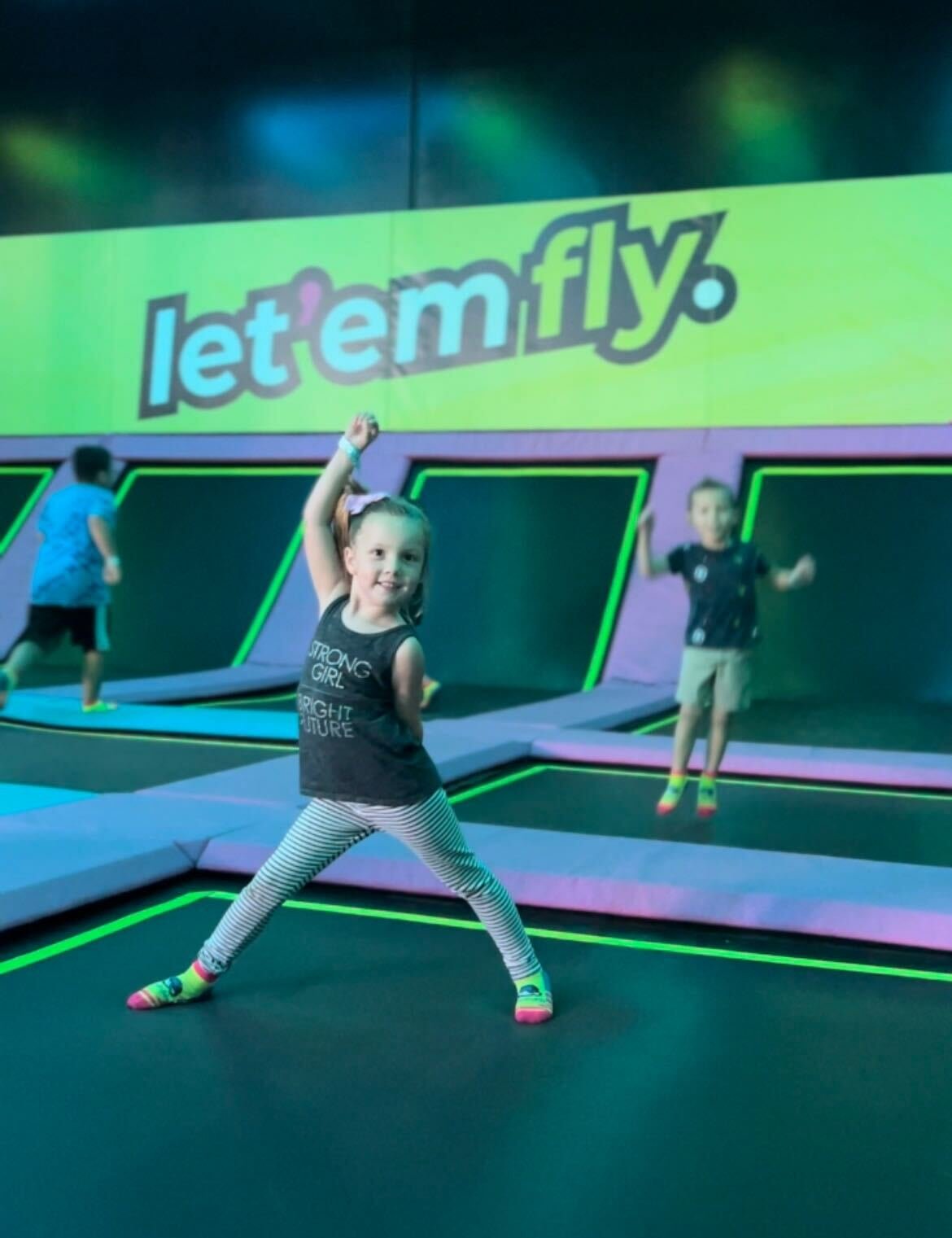 girl on trampoline with let em fly text on green wall
